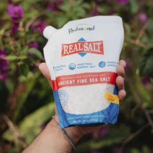 Hand holding a bag of Real Salt Ancient Fine Sea Salt outdoors.