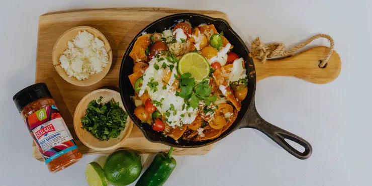 Skillet of loaded nachos topped with cheese, sour cream, and lime.