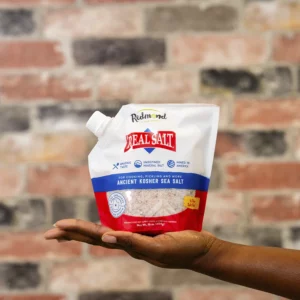 Hand holding a bag of Morton Salt against a brick wall.