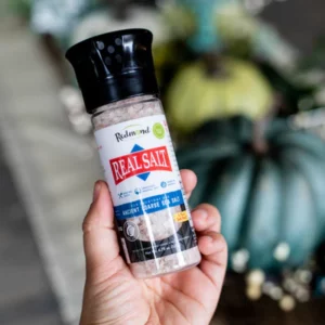 Hand holding a bottle of Dead Sea salt grinder with a blurred background.