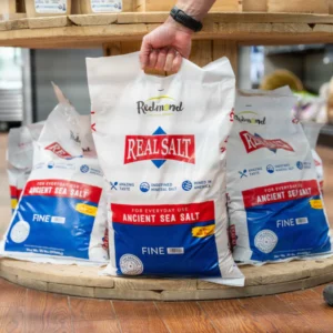 A hand holding a Real Salt package with other salt bags in the background.