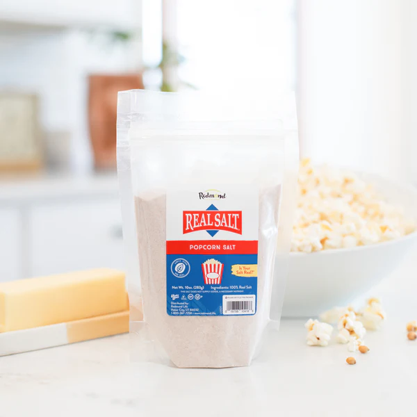A container of Great Value popcorn salt on a kitchen counter with popcorn.