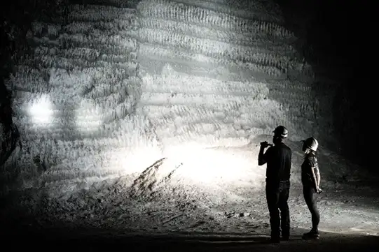 Two people standing near a massive snow wall at night.
