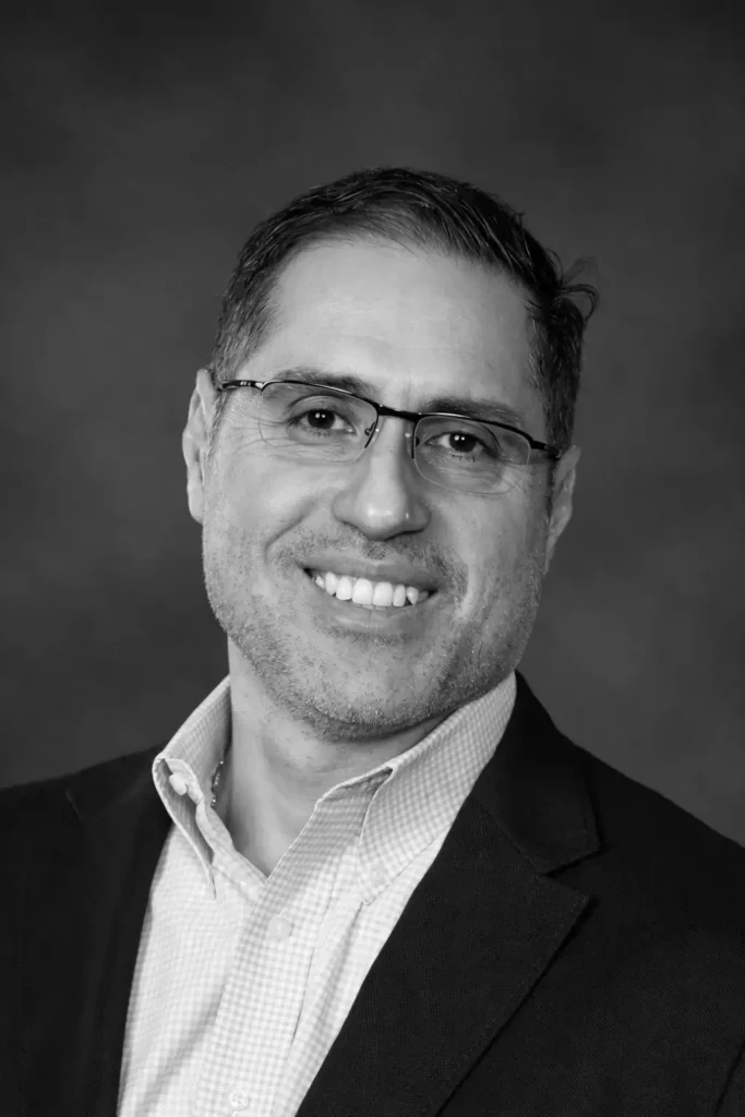 Smiling man in glasses and suit against a plain backdrop.